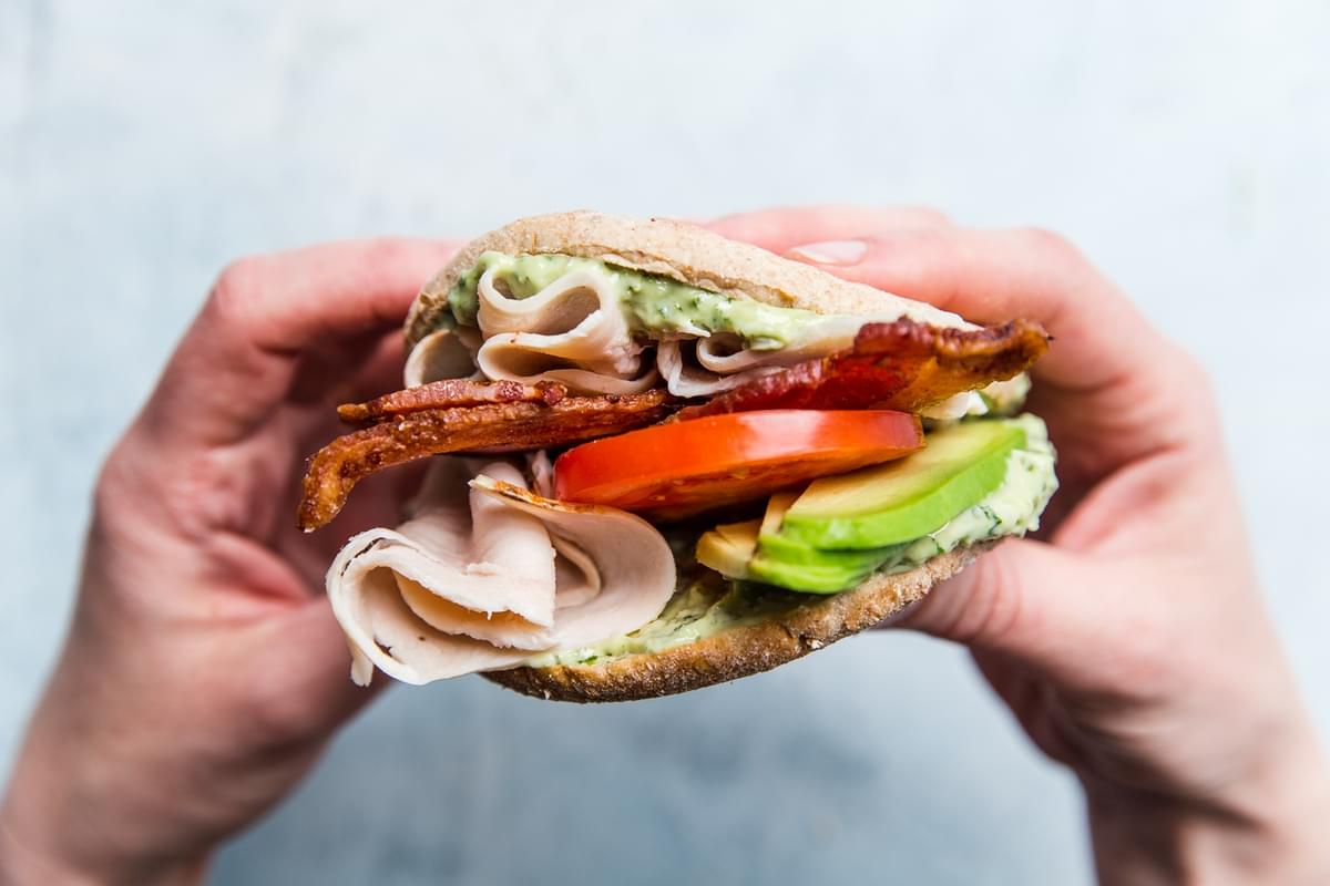 hand holding Turkey Bacon Club Sandwich with tomato avocado and pesto mayonnaise