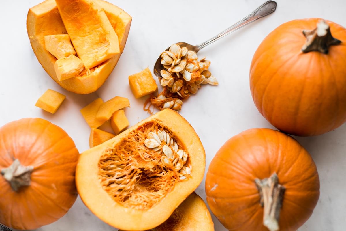 small pumpkins cut in half with a spoon filled with pumpkins seeds