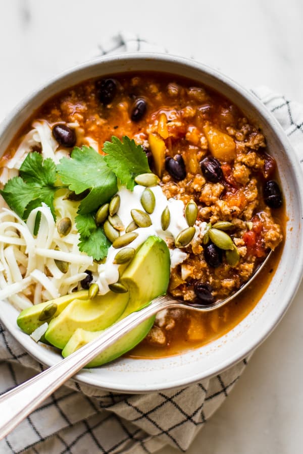 bowl of easy turkey pumpkin chili topped with cheese, sour cream, fresh cilantro, avocados and pumpkin seeds