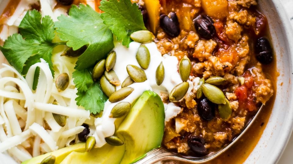 bowl of easy turkey pumpkin chili topped with cheese, sour cream, fresh cilantro, avocados and pumpkin seeds