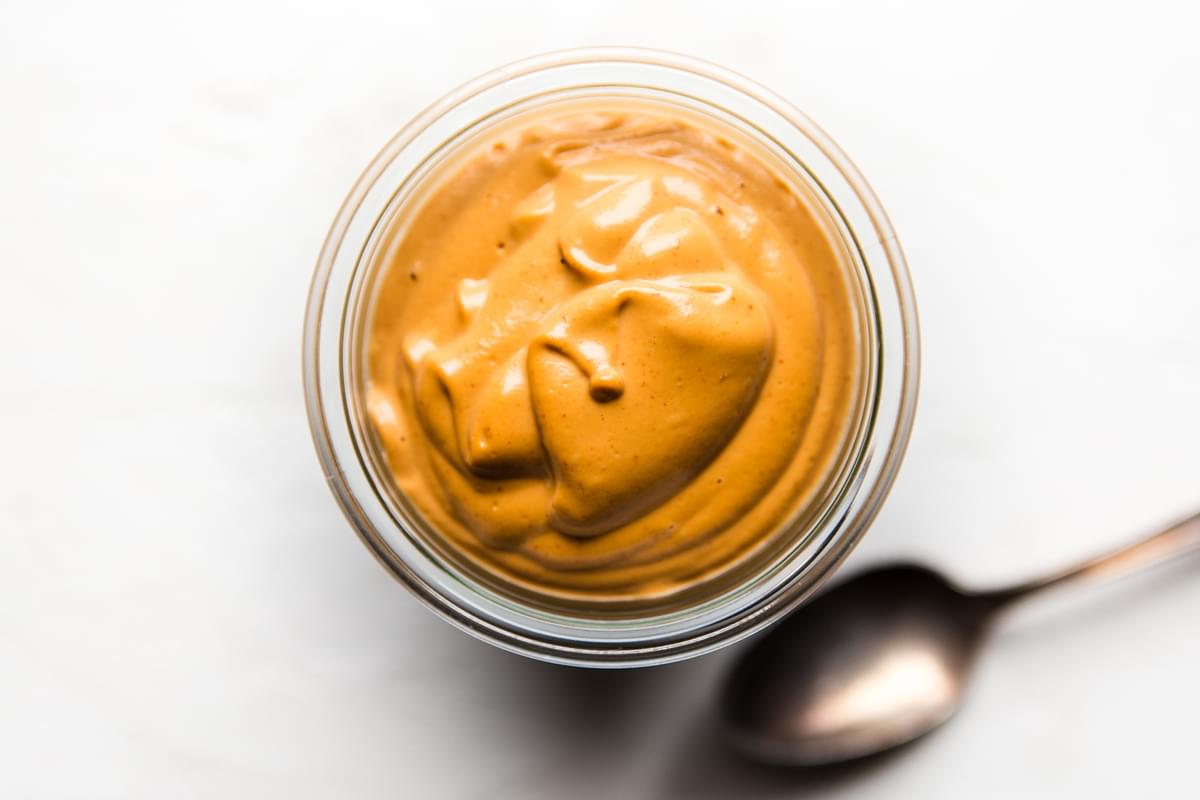 homemade vegan cashew cheese sauce in a jar next to a spoon