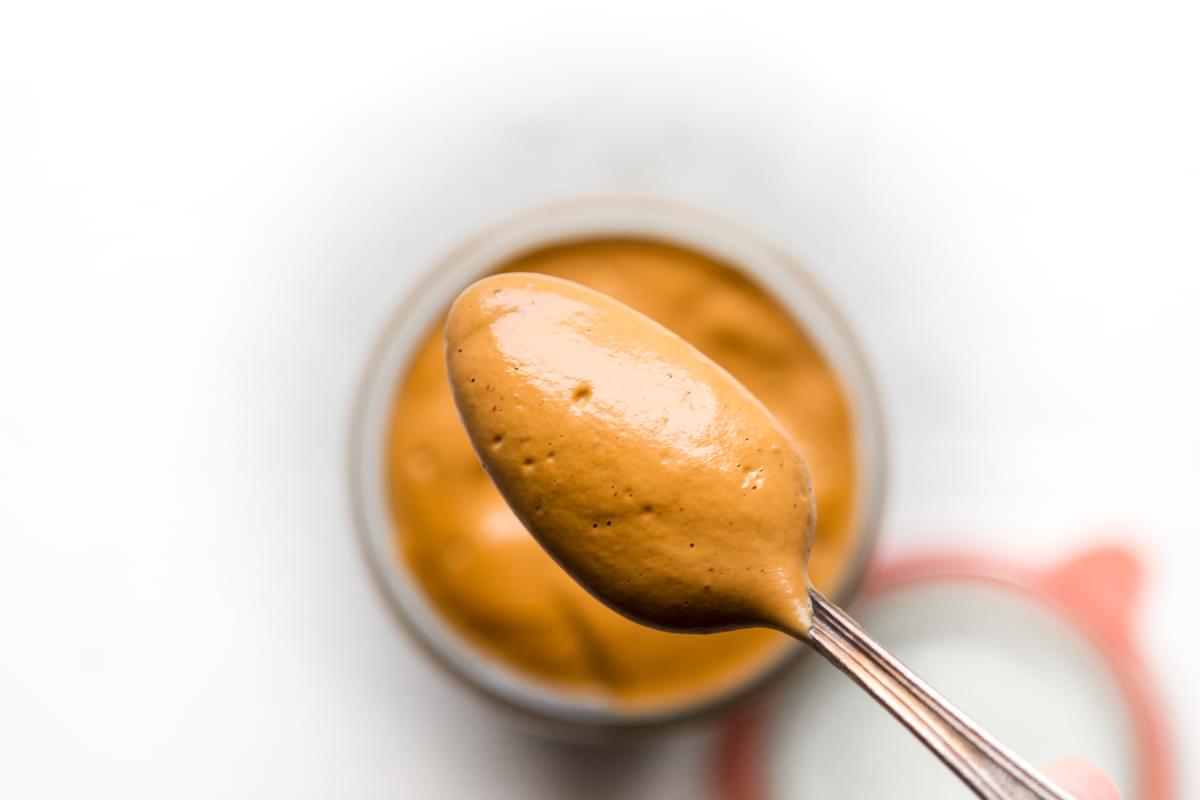 homemade Vegan Cashew Cheese Sauce being scooped out of a jar with a spoon