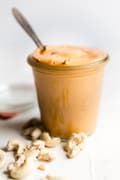 homemade vegan cashew cheese sauce in a jar on the counter topped next to a spoon for scooping