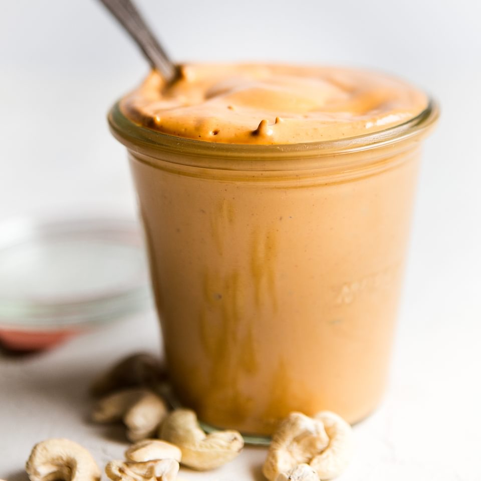 Vegan cashew cheese in a jar with a spoon and some raw cashews