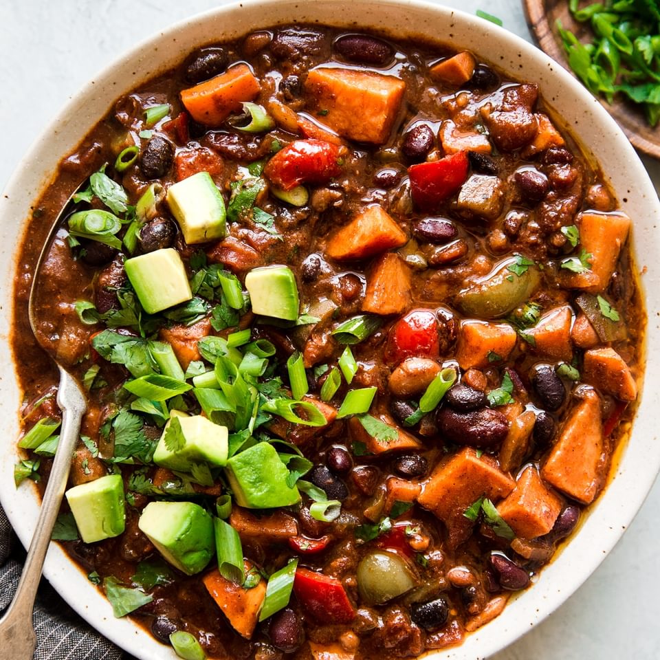 A big bowl of vegetarian chili with avocado and sweet potatoes with a spoon