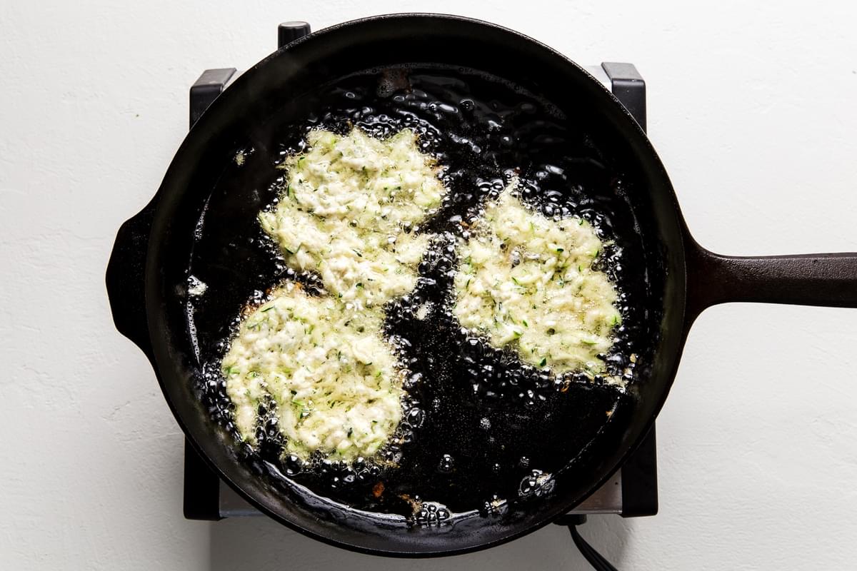 Zucchini Fritters frying in oil in a cast iron skillet