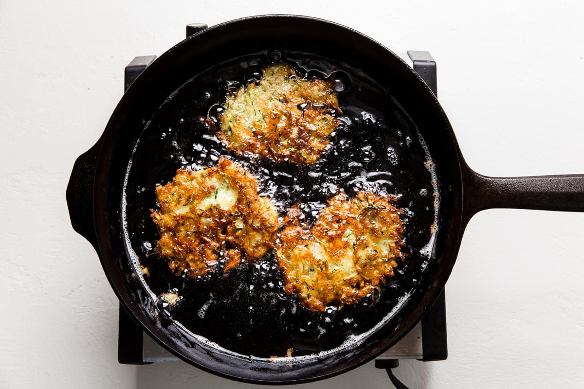 Zucchini Fritters frying in a cast iron pan