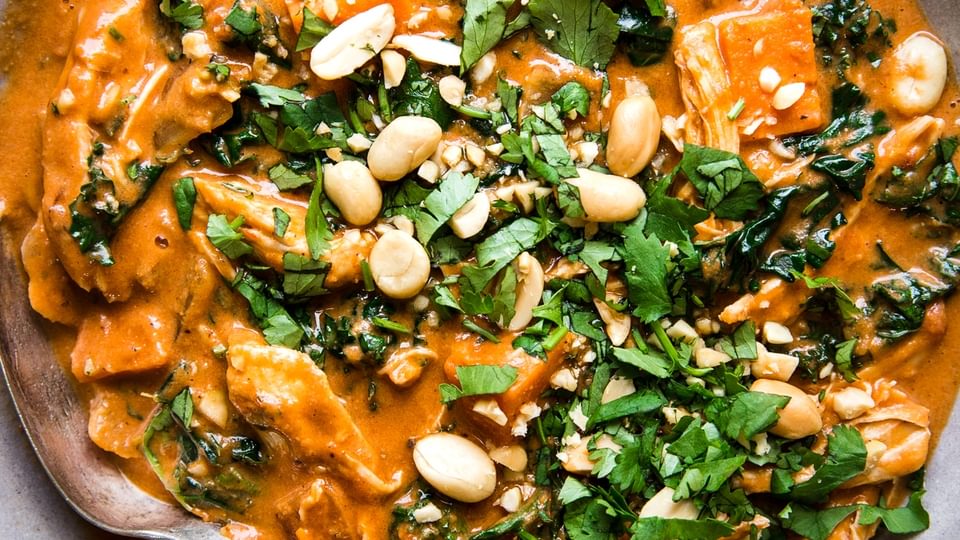 African Peanut Soup in a bowl with ginger, garlic, cumin, crushed tomatoes, sweet potatoes, chickpeas, chicken, kale.