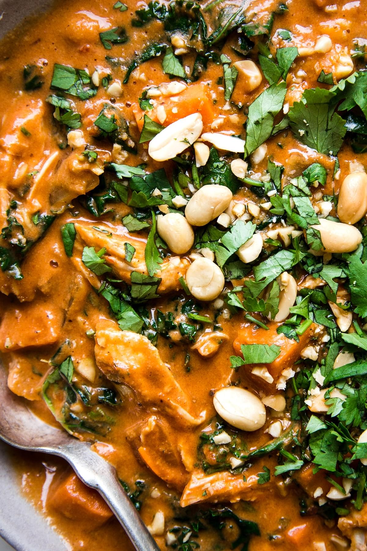 sweet and spicy peanut soup with chicken kale chickpeas and sweet potatoes garnished with cilantro and peanuts.