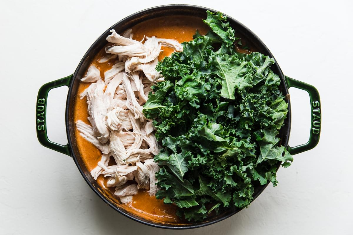 chicken and kale being added peanut butter soup recipe in a soup pot