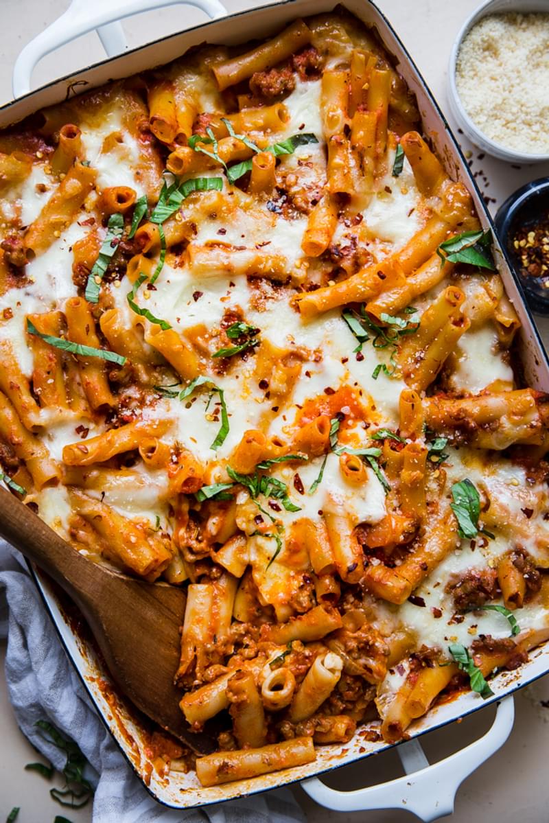 baked ziti in a baking dish topped with fresh basil and parmesan