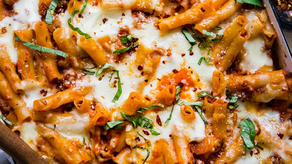 baked ziti in a baking dish topped with fresh basil and parmesan