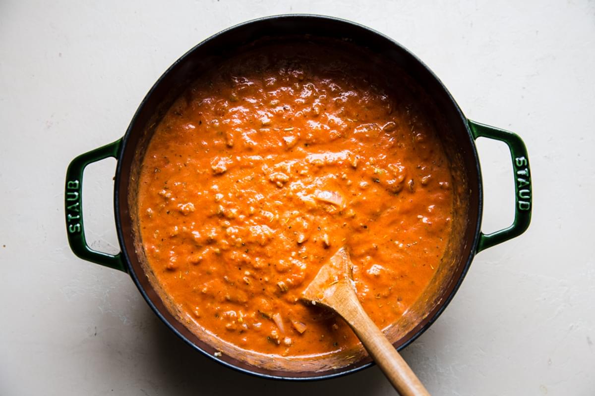 ground sausage and homemade creamy tomato sauce being stirred in a pot with a wooden spoon