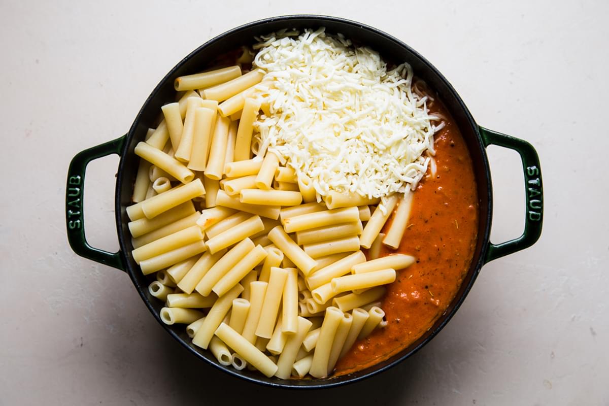 ziti pasta and mozzarella cheese being added to a pot with homemade ziti sauce and ground sausage