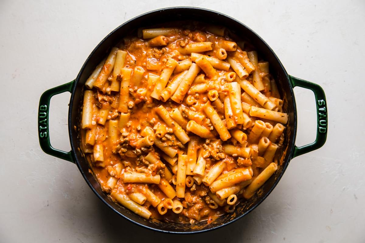 ziti pasta in a dutch oven with marinara, pasta, mozzarella and basil