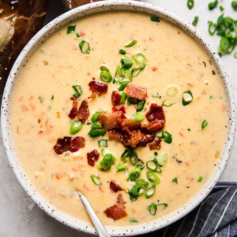 Beer Cheese Soup with bacon, peppers in a bowl with pretzel rolls and a spoon