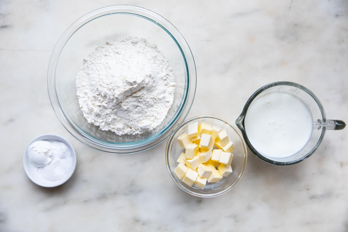 Flour, butter, baking powder, baking soda, salt and buttermilk in bowls on the counter for homemade buttermilk biscuits