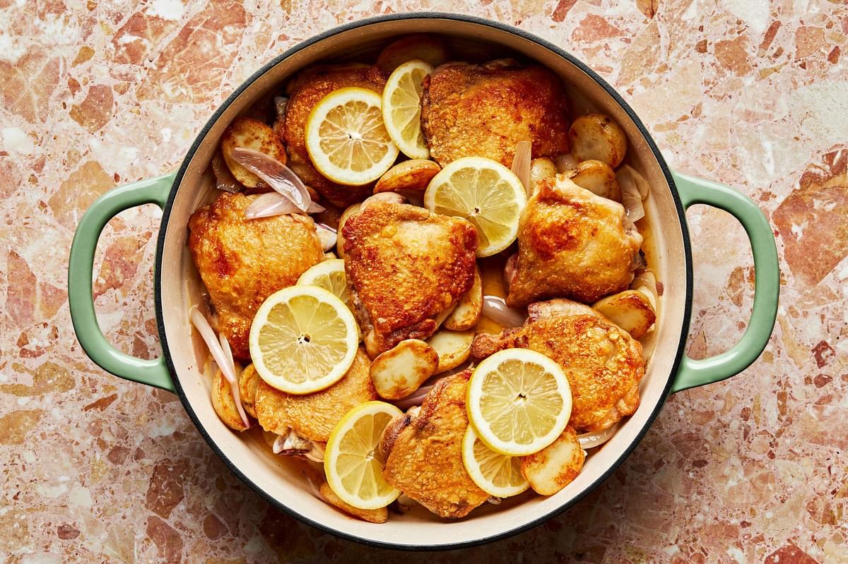 lemon slices added to a pan with braised chicken, roasted potatoes, shallots, garlic, chicken and stock.