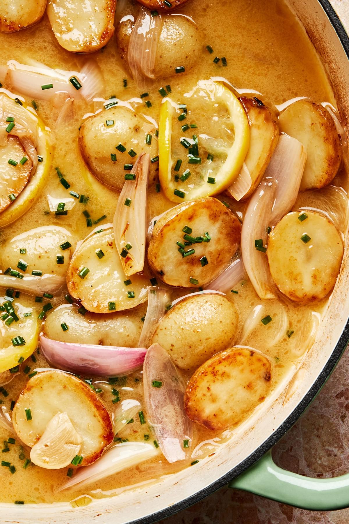 Close up of Roasted potatoes and shallots in a braising dish with with a lemon and chive butter sauce