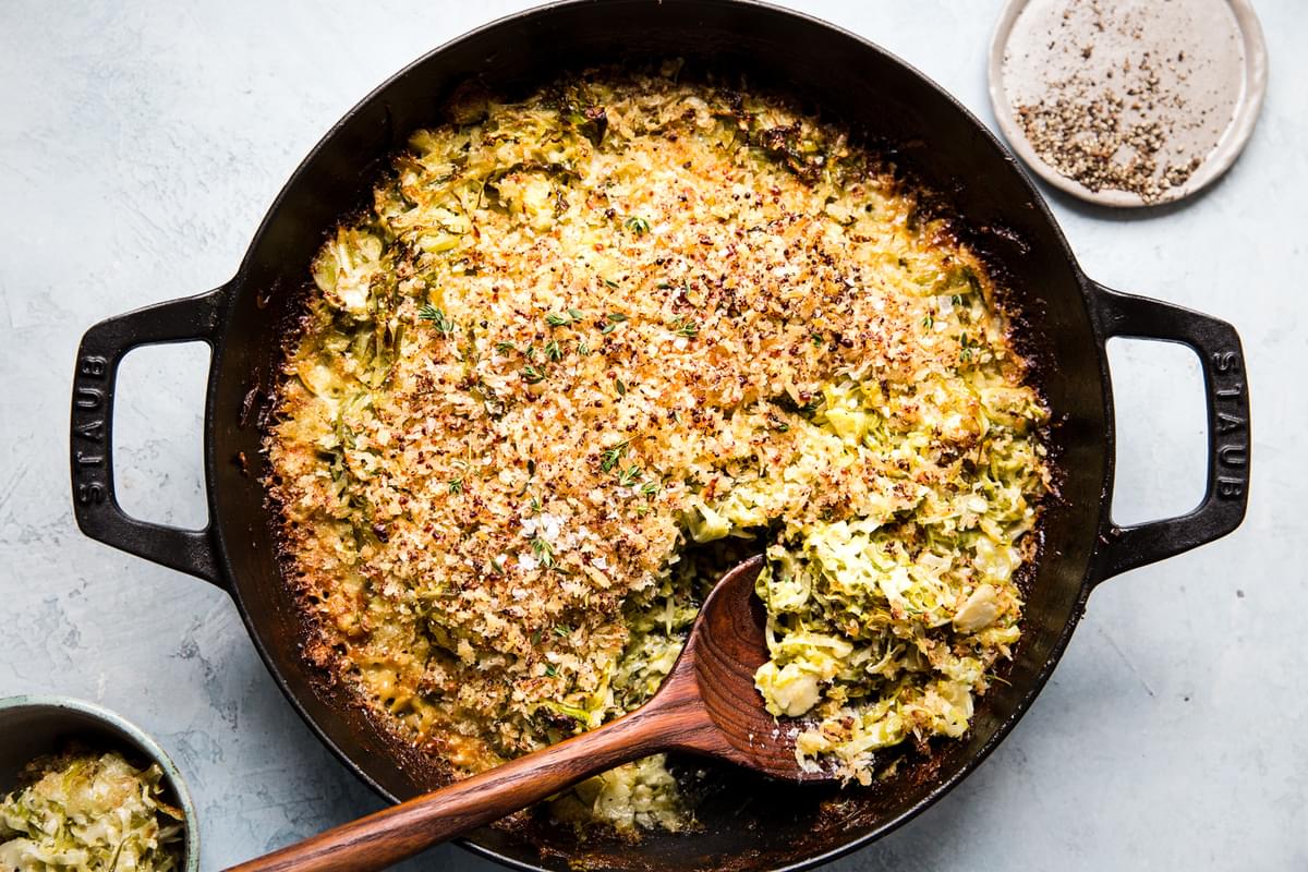 a spoon scooping Brussels sprouts gratin with toasted bread crumbs from a baking dish