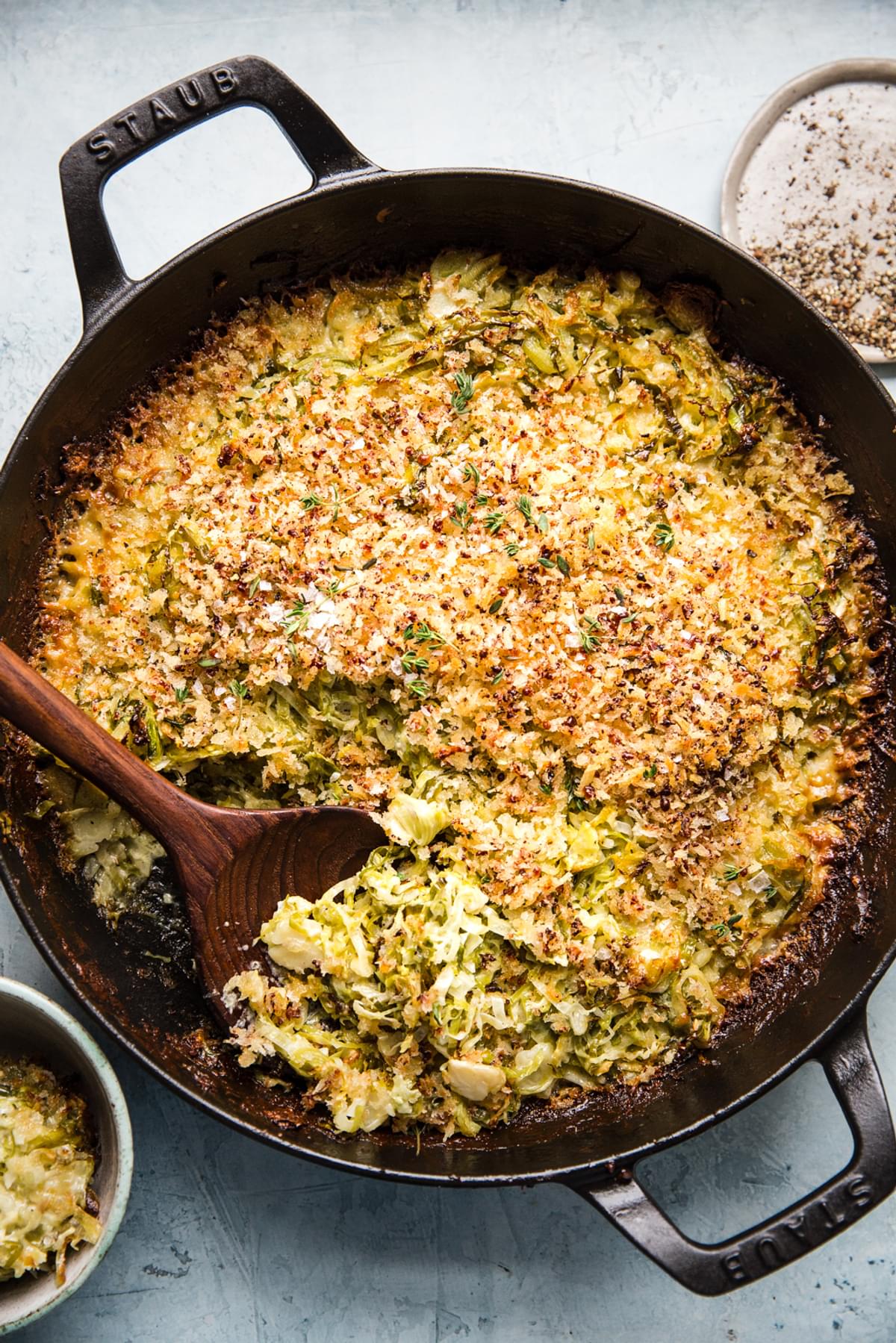 creamy Brussels Sprout au Gratin in a skillet sprinkled with bread crumbs with a wooden spoon