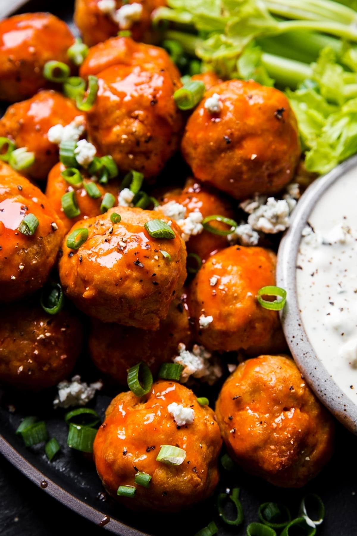 Buffalo chicken meatballs on a plate with a small bowl of blue cheese dressing and celery