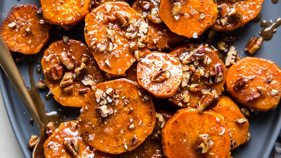 sliced Candied Yams with Honey and Brown Sugar and pecans on a platter with a serving spoon