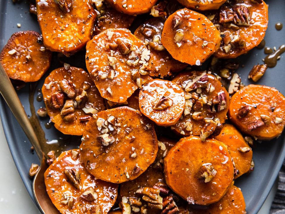 sliced and roasted Candied Yams with Honey, Brown Sugar and pecans on a platter with a serving spoon