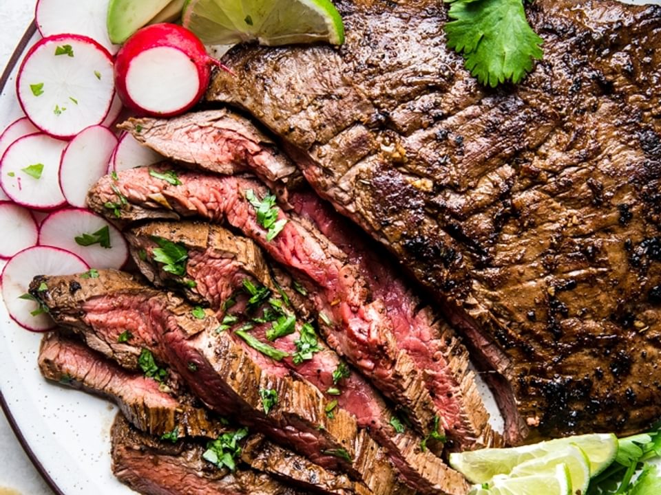 A plate of carne asada with tortillas, limes, avocado and radishes