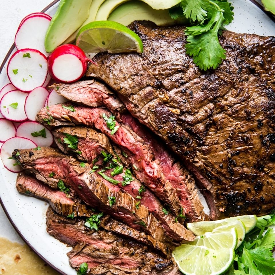 A plate of carne asada with tortillas, limes, avocado and radishes