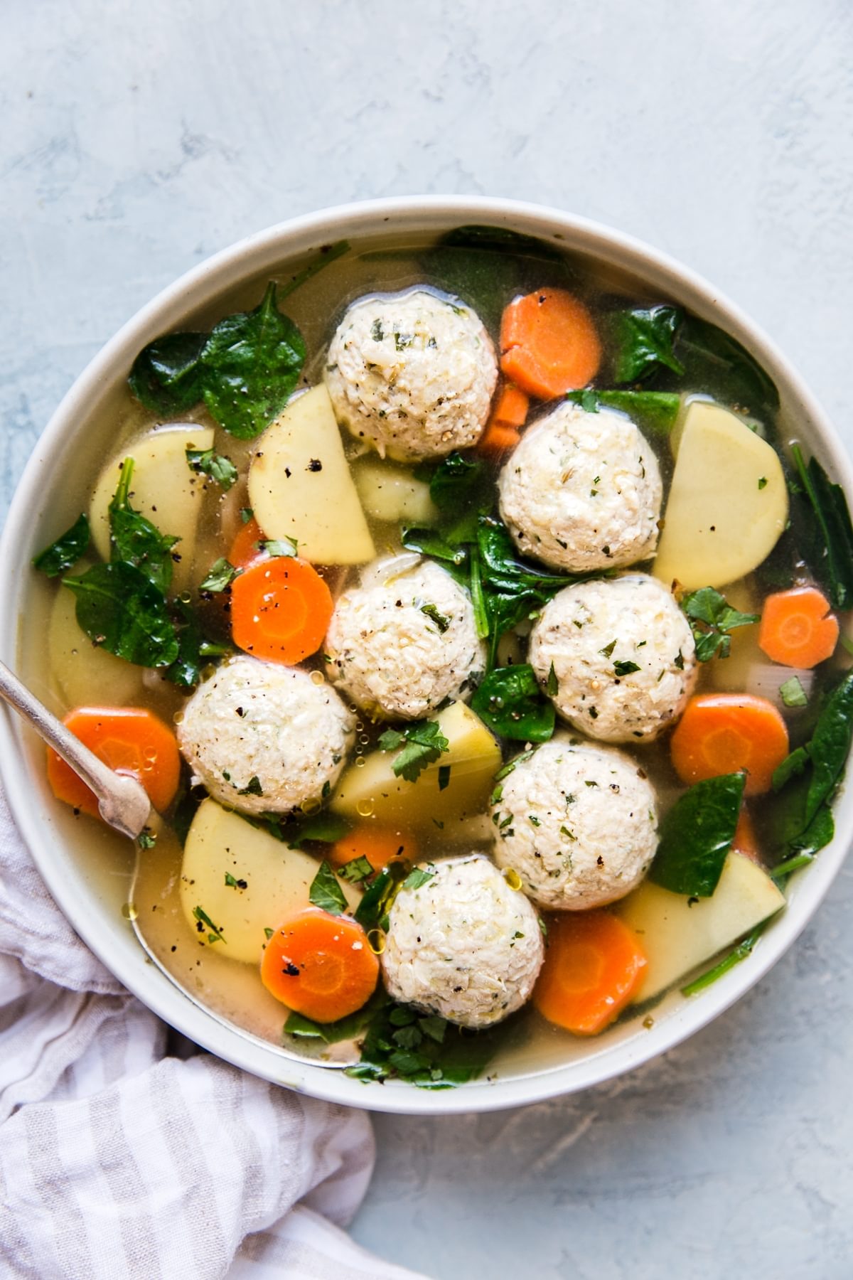 A bowl of chicken meatball soup with carrots, potatoes and kale