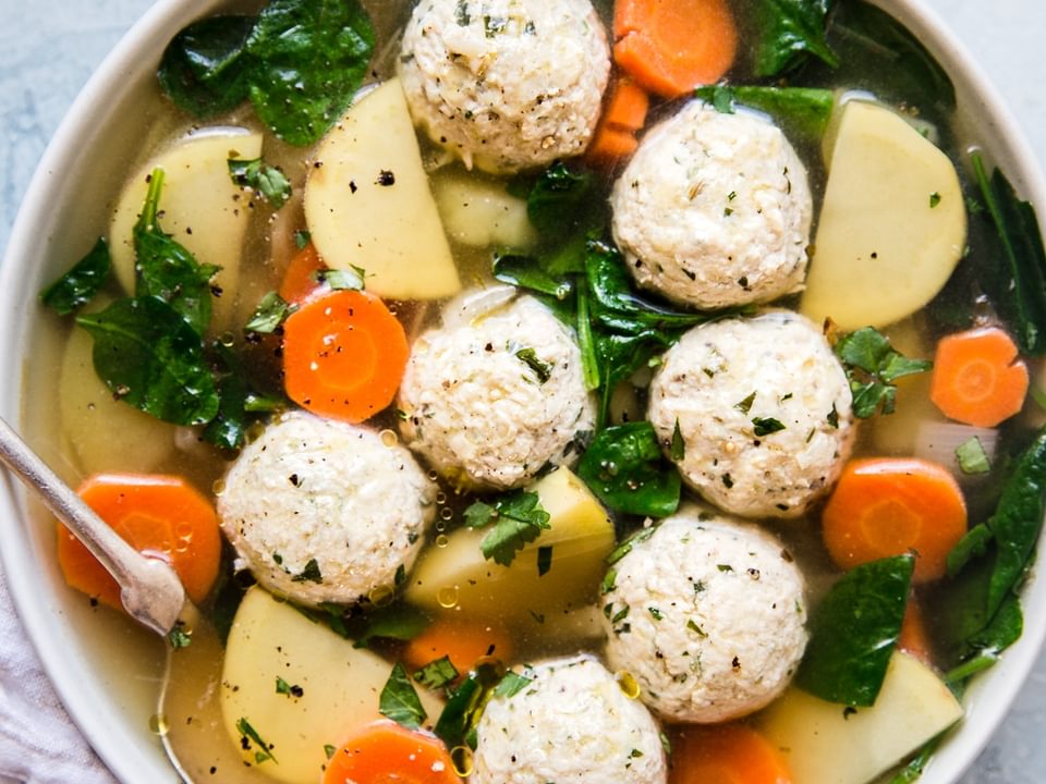 A bowl of chicken meatball soup with carrots, potatoes and kale