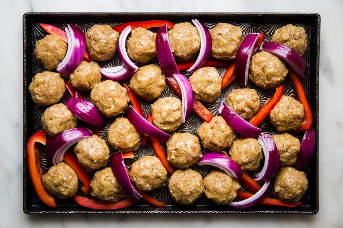 raw chicken shawarma meatballs with red onions and bell peppers on a baking sheet