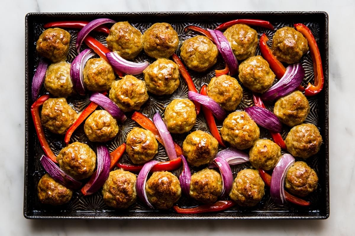 Baked chicken shawarma meatballs shown on a baking sheet with bell peppers and red onions.