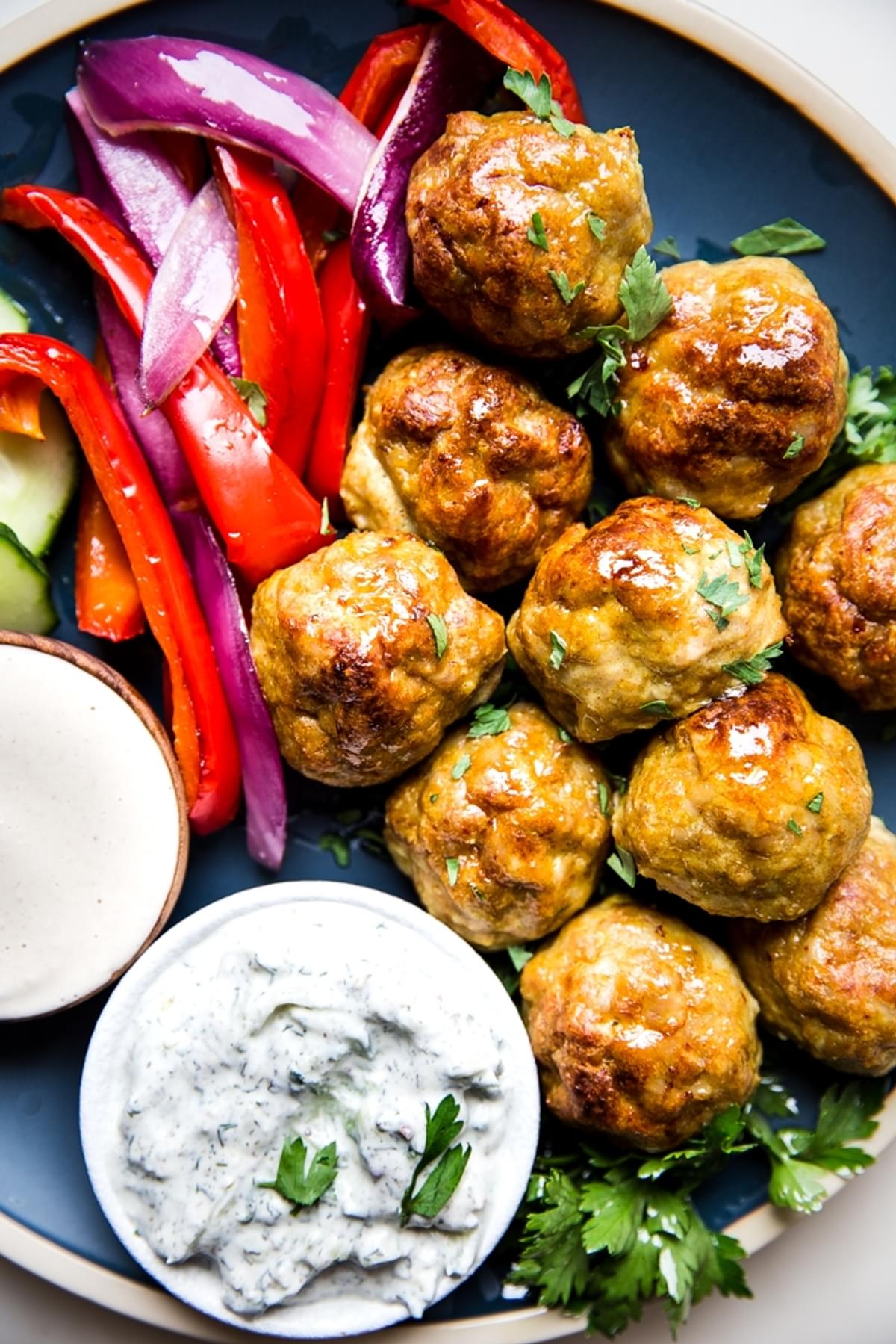 chicken shawarma meatballs shown on a blue plate with herbs and vegetables
