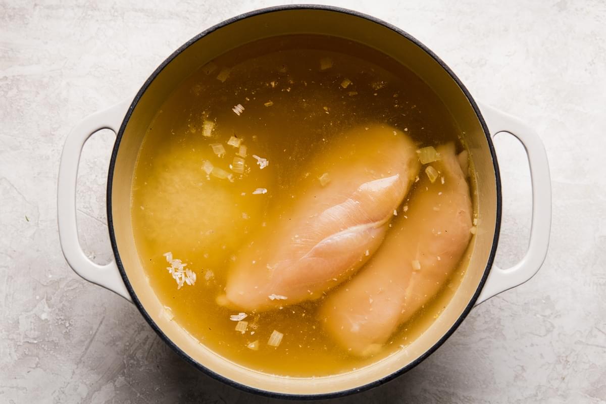 two raw chicken breast and rice added to a pot of chicken stock with onion and garlic.