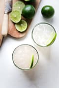 two classic margaritas in glass cups next to a wooden cutting board with sliced limes