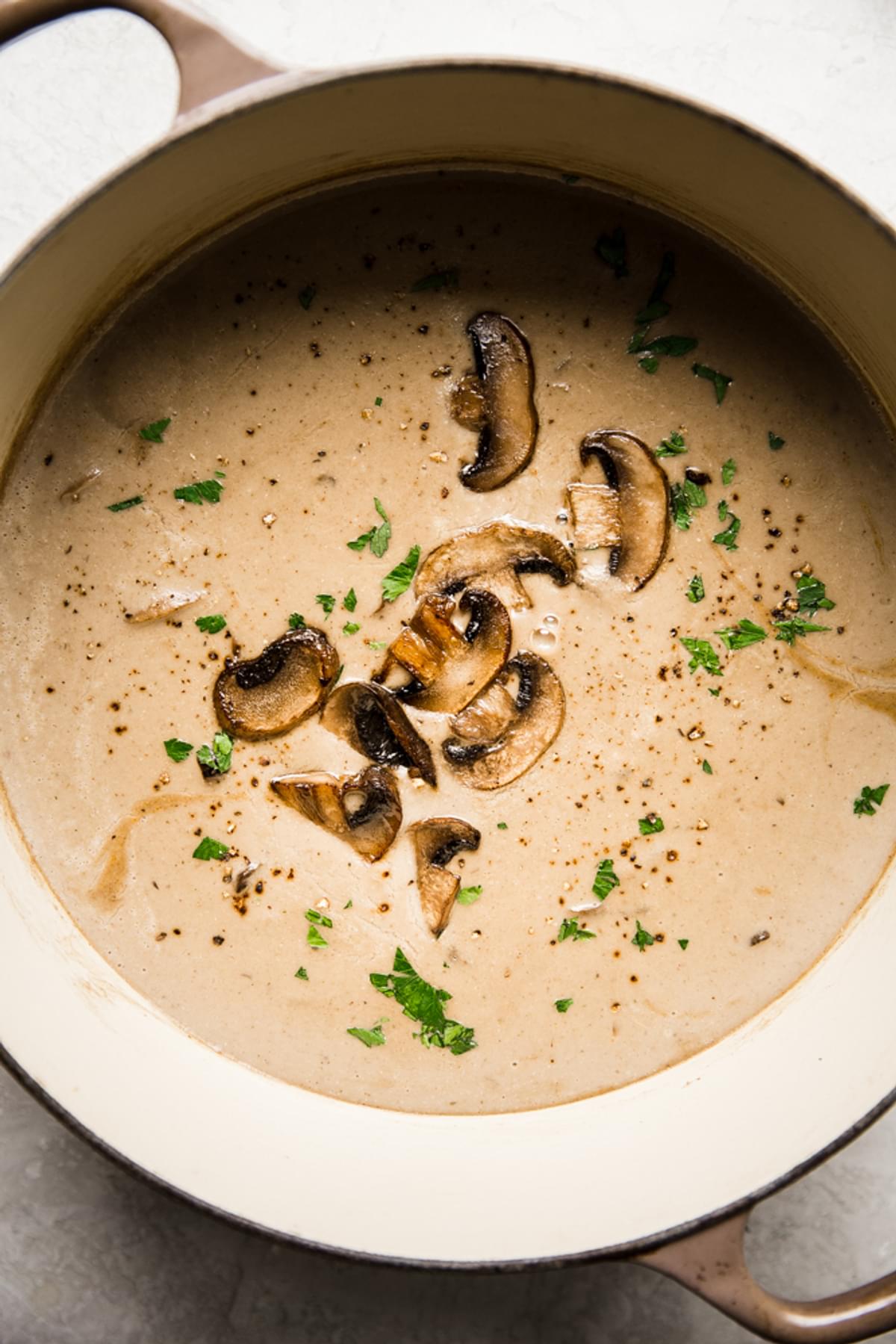 a pot of homemade cream of mushroom soup with heavy cream parsley, onions and garlic in a bowl