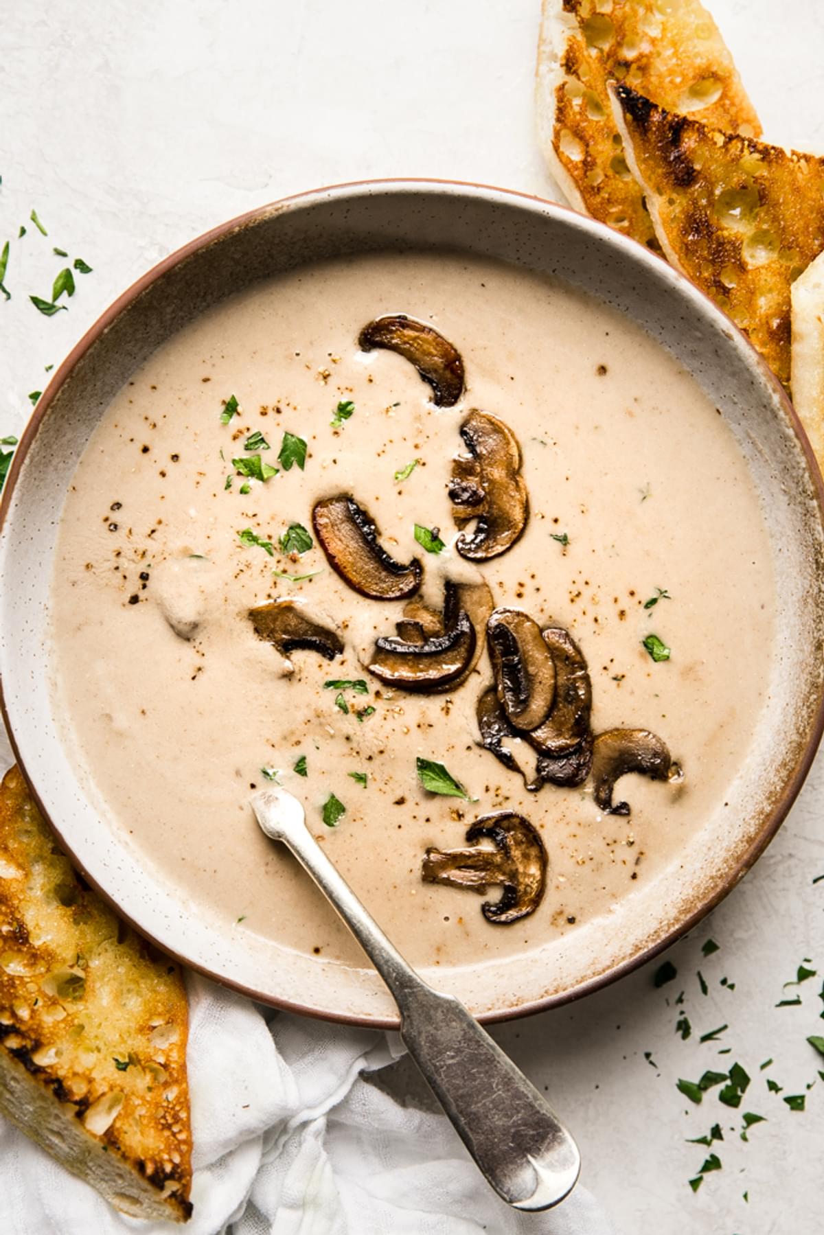 a bowl of homemade cream of mushroom soup with heavy cream parsley, onions and garlic being served with crusty bread