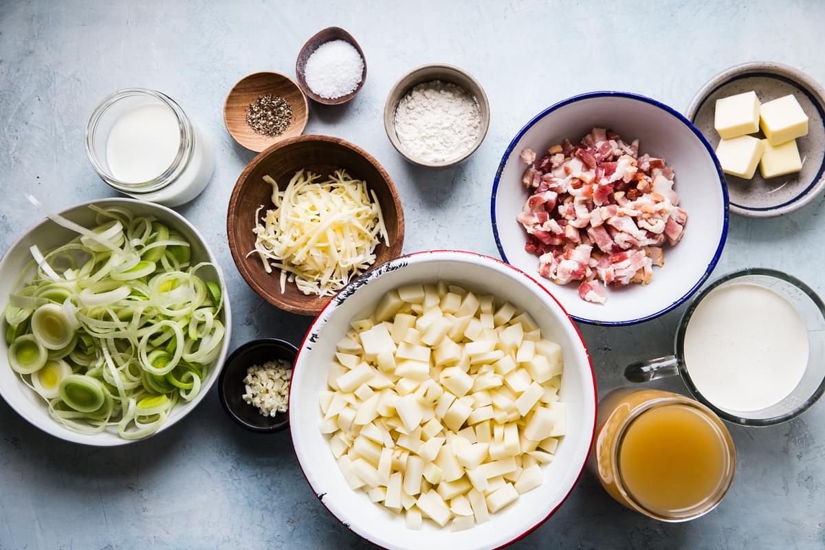 ingredients laid out for creamy potato soup with leeks, bacon, chicken stock, butter, flour, cheddar cheese, garlic, salt