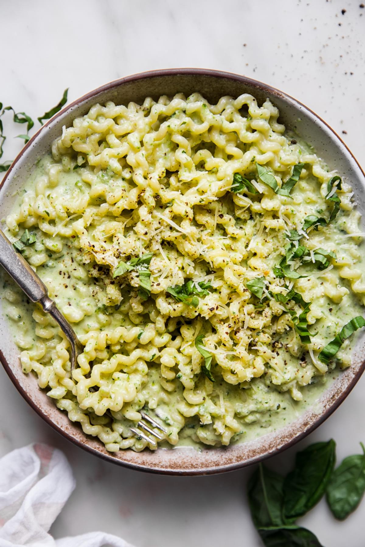 creamy zucchini pasta sauce with spiral pasta in a bowl with parmesan cheese and fresh basil.