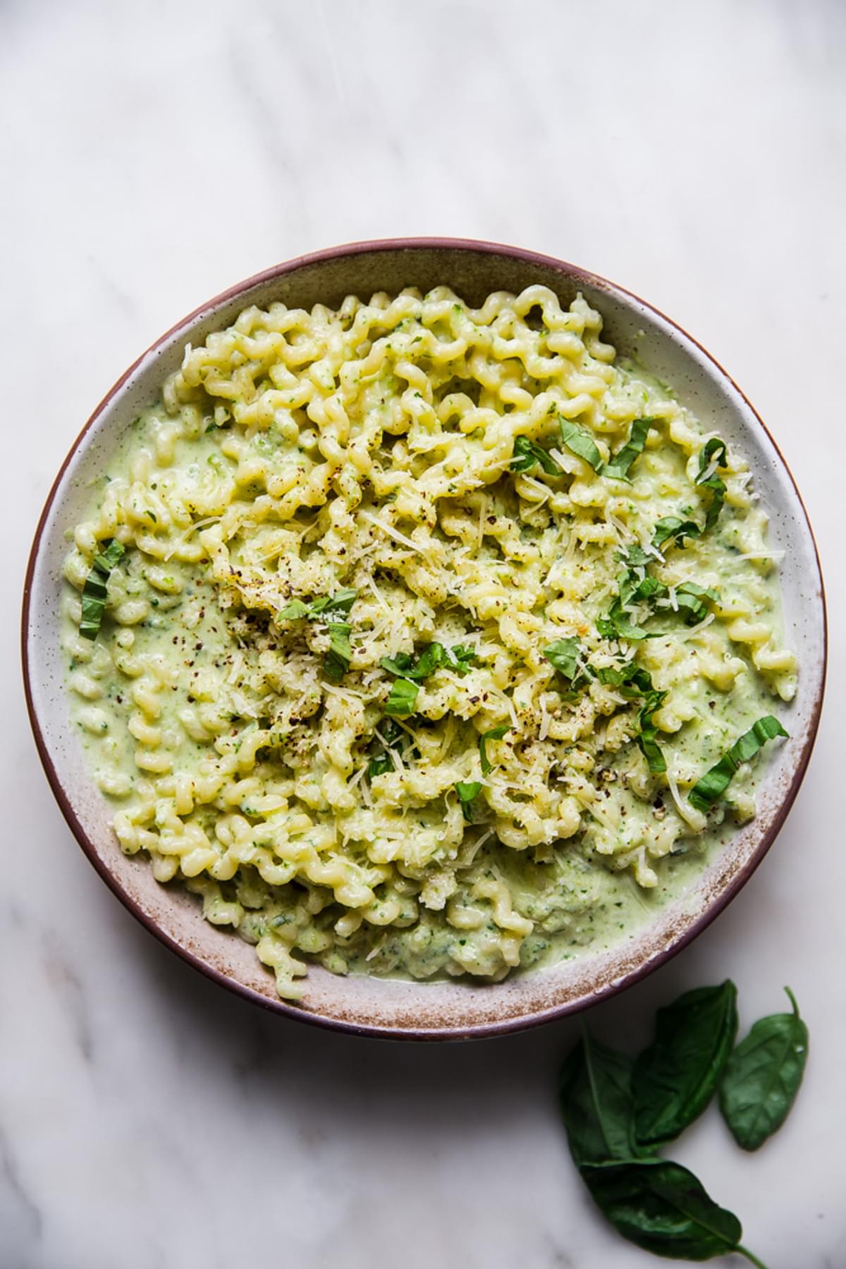creamy zucchini pasta sauce with spiral pasta in a bowl with parmesan cheese and fresh basil.