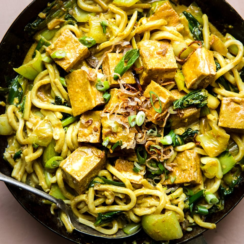 crispy tofu with creamy curry udon noodles in a saucepan with a serving spoon