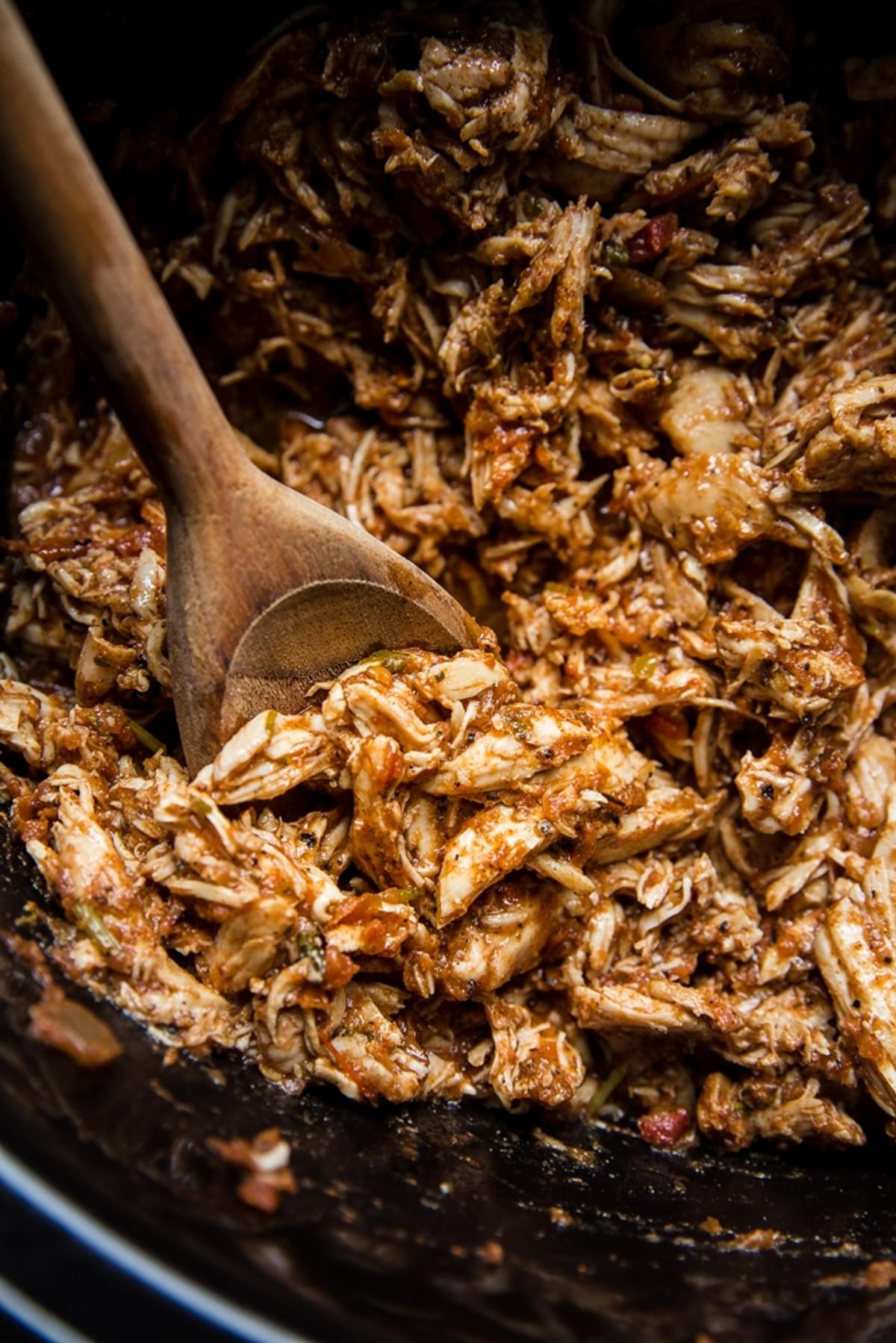 crock pot chicken taco meat shown shredded in a crockpot with a wooden spoon