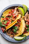 crock pot chicken tacos in a silver pan topped with salsa and limes