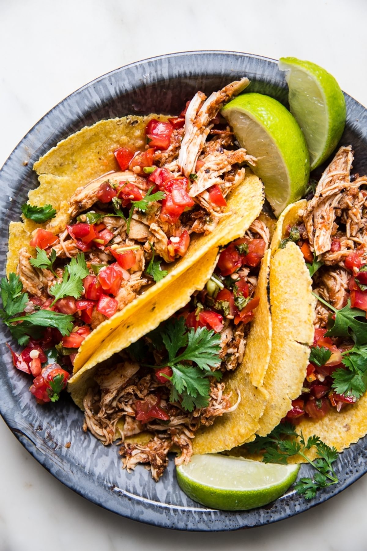 crock pot chicken tacos in a silver pan topped with salsa and limes
