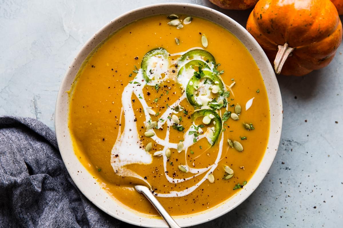 Ceramic bowl filled with pumpkin soup topped with jalapenos, coconut milk, pumpkin seed and black pepper