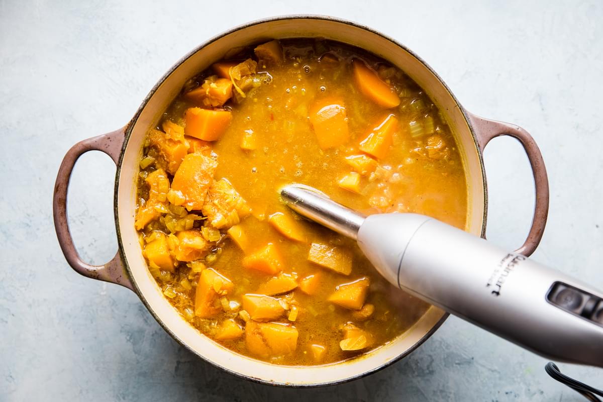 curried pumpkin soup in a large soup pot being blended with a hand blender