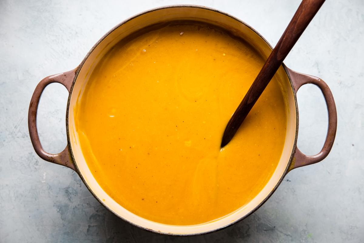 pumpkin soup blended in a large pot with a wooden spoon
