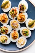 blue plate with deviled eggs topped with radishes, pickled onions, bacon and pickles